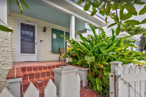 A charming house entrance with a porch, green plants, and a white picket fence.