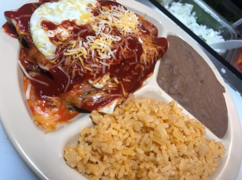 A plate of enchiladas topped with cheese and sauce, served with refried beans and rice.