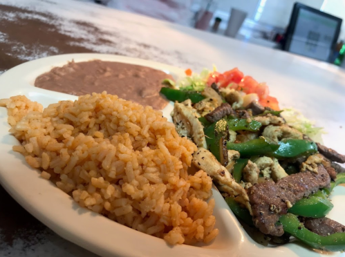 A plate of rice, refried beans, and grilled chicken with green peppers and tomatoes on a bed of lettuce.