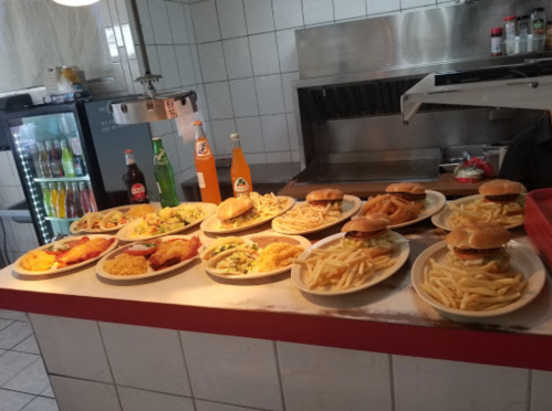 A variety of plates with burgers, fries, and colorful drinks arranged on a counter in a casual dining setting.