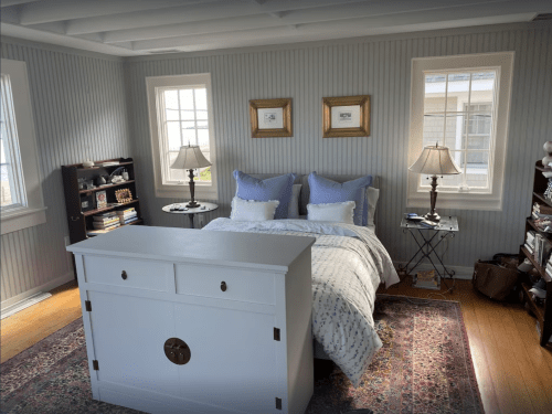 A cozy bedroom featuring a white bed with blue pillows, two lamps, and a bookshelf against the wall.