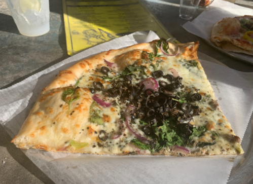 A slice of pizza topped with black olives, greens, and red onions on a white plate.