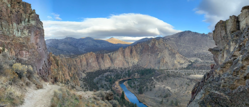 A panoramic view of rugged cliffs and a winding river surrounded by mountains under a partly cloudy sky.