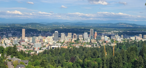 A panoramic view of Portland, Oregon, showcasing the skyline amidst lush green trees and distant mountains.