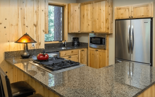 Cozy kitchen with wooden cabinets, granite countertops, stainless steel appliances, and a window overlooking nature.