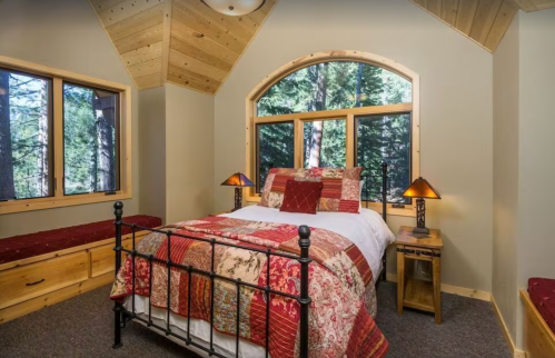 Cozy bedroom with a large window, wooden accents, and a patterned bedspread, surrounded by trees.