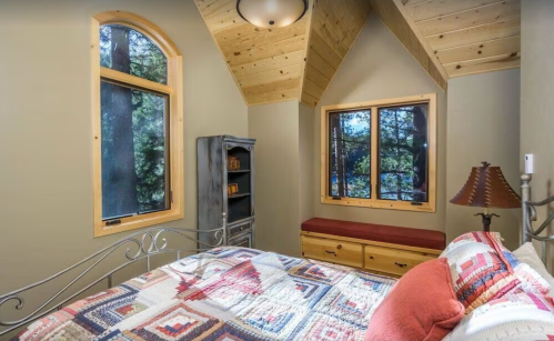 Cozy bedroom with a quilted bed, wooden accents, and large windows showcasing a forest view.