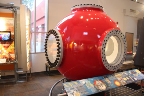 A large red underwater exploration sphere displayed in a museum, with informational panels nearby.