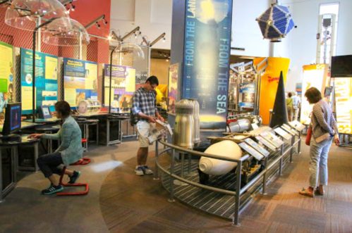 Visitors explore interactive exhibits in a science museum, featuring displays on ocean and space exploration.