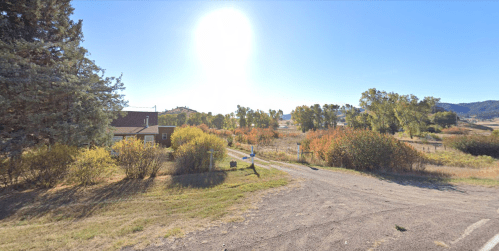 A sunny rural scene with a dirt road, trees, and a house surrounded by colorful foliage.