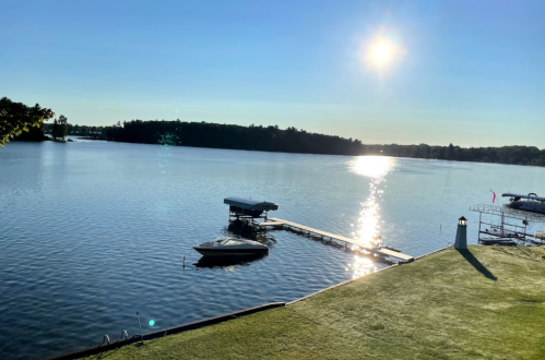 A serene lake view at sunrise, with a dock, boats, and sunlight reflecting on the water's surface.