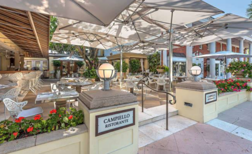 Outdoor dining area of Campiello Ristorante, featuring tables, umbrellas, and vibrant flowers in a sunny setting.