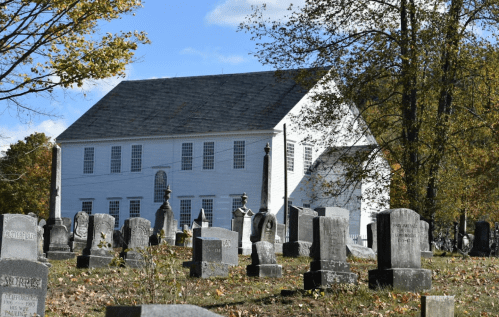 A historic white building behind a cemetery with various gravestones under a clear blue sky.