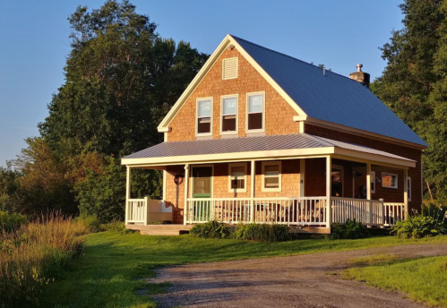 A charming two-story house with a porch, surrounded by greenery and bathed in warm sunlight.