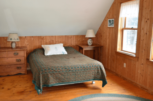 Cozy bedroom with wooden walls, a bed covered in a patterned blanket, and two lamps on bedside tables.