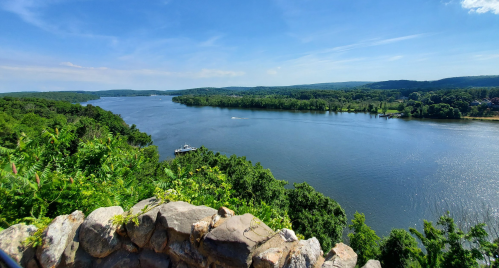 A scenic view of a river surrounded by lush greenery under a clear blue sky.