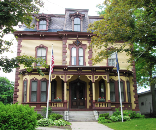 Victorian-style house with yellow and maroon exterior, featuring ornate details, large windows, and a front porch.