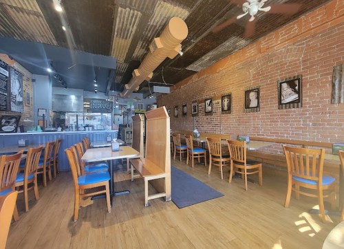 Interior of a restaurant featuring wooden tables, blue chairs, exposed brick walls, and framed photos.
