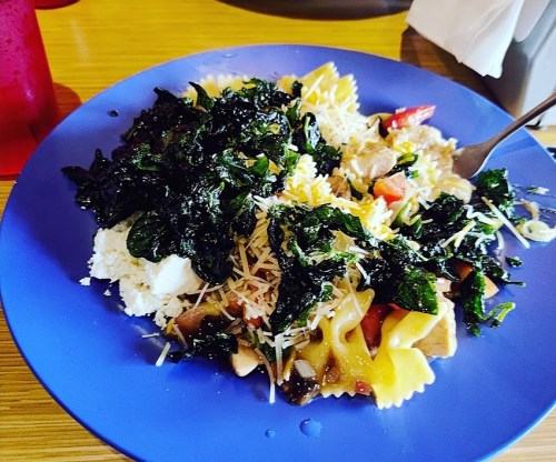 A blue plate filled with pasta, cheese, vegetables, and a generous serving of crispy kale.