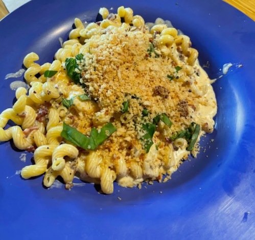 A blue plate with creamy pasta topped with breadcrumbs and fresh basil.