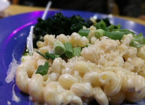 A plate of creamy pasta topped with green onions, alongside a serving of dark leafy greens.