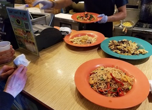 A counter with plates of colorful pasta dishes and a person serving food in a casual dining setting.