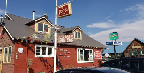 A rustic red building with signs for beer, groceries, and gasoline, set against a clear blue sky.