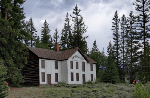 A rustic, two-story building with a sign reading "Interlake" surrounded by tall trees and a cloudy sky.