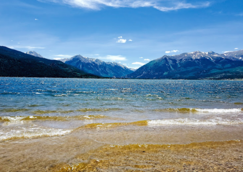 A serene lake with gentle waves, surrounded by mountains under a clear blue sky.