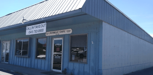 Exterior of a blue building with a metal roof, featuring signs for "Callin' Takeout" and "Potbelly Cafe."