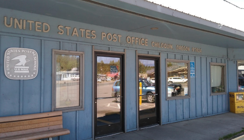 Exterior of the United States Post Office in Chiloquin, Oregon, featuring a blue wooden facade and large glass doors.