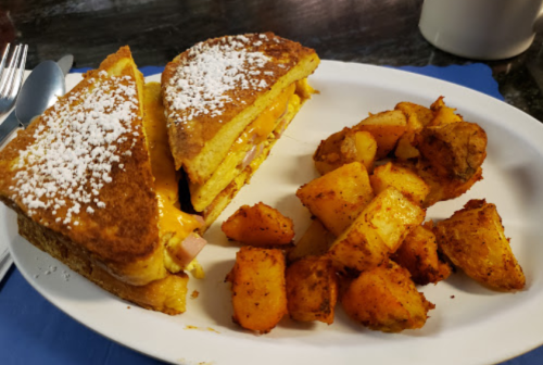 A plate featuring a grilled cheese sandwich dusted with powdered sugar and a side of seasoned roasted potatoes.