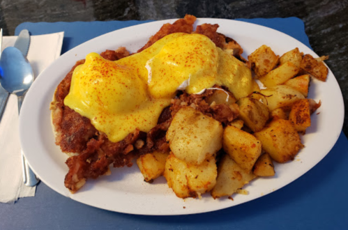 A plate of fried fish topped with yellow sauce, served with seasoned roasted potatoes on the side.