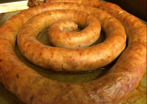 A large, spiral-shaped sausage resting in a pan, showcasing its golden-brown color and juicy texture.