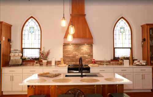 Modern kitchen with a brick backsplash, wooden accents, and stained glass windows, featuring pendant lights and a large island.
