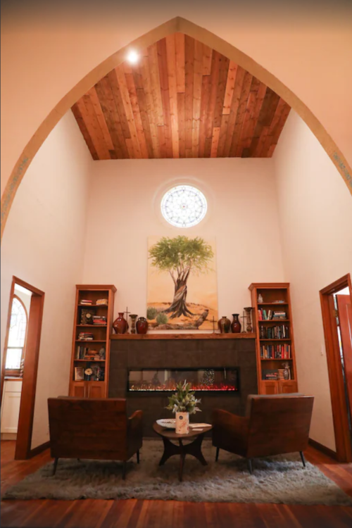 Cozy living room with high arched ceiling, wooden accents, a large tree painting, and two armchairs by a stone fireplace.