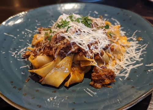 A plate of pappardelle pasta topped with shredded meat and grated cheese, garnished with fresh herbs.