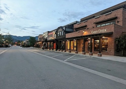 A quiet street lined with brick buildings at dusk, featuring shops and mountains in the background.