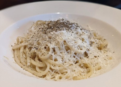 A plate of spaghetti topped with grated cheese and black pepper, served in a white bowl.