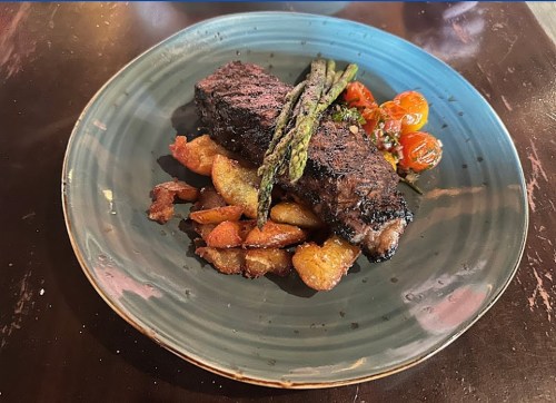 A plate featuring grilled steak, roasted potatoes, asparagus, and cherry tomatoes, served on a blue dish.