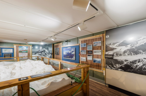 A museum exhibit featuring a topographical model of mountains, with informational panels and photographs on the walls.