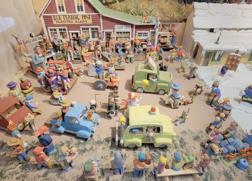 A colorful miniature scene depicting a bustling town square with figurines, cars, and buildings in a playful setting.