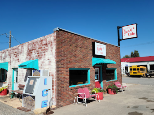 A brick building with teal awnings, featuring a sign for Jacoby's Cafe and outdoor seating. Clear blue sky above.