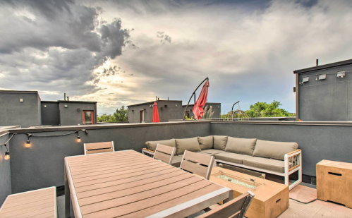 Rooftop patio with a dining table, seating area, and umbrellas, set against a cloudy sky.