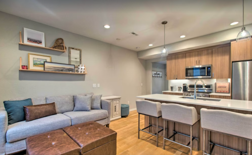 Modern kitchen and living area featuring a sofa, ottoman, and sleek appliances with warm lighting.