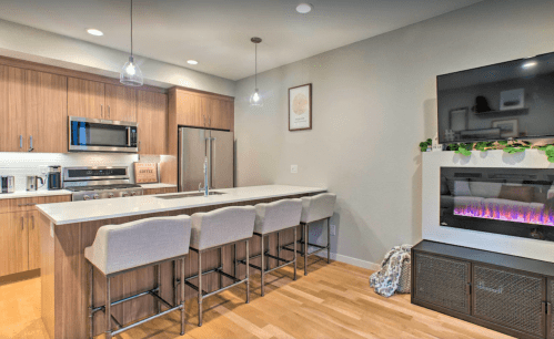 Modern kitchen with wood cabinets, stainless steel appliances, a large island with bar stools, and a cozy electric fireplace.