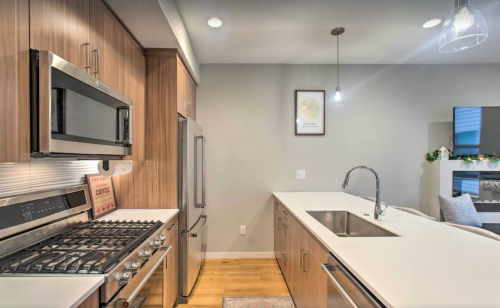 Modern kitchen with stainless steel appliances, a large island, and warm wood cabinetry, featuring pendant lighting.
