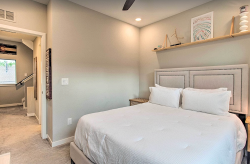 Cozy bedroom featuring a queen bed, light gray walls, and modern decor with a shelf and artwork.