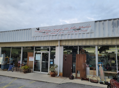 Exterior of a shop with a sign reading "Norfleet Trading Antiques & Flea Market," featuring large windows and an open door.