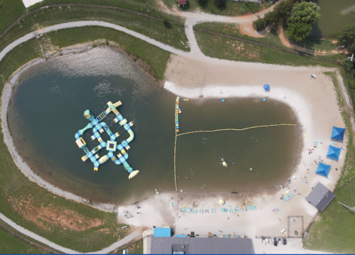 Aerial view of a water park with inflatable structures, a sandy beach area, and people enjoying the water.